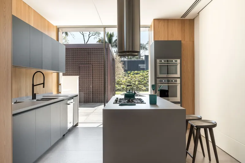 Kitchen with island and stainless steel hood beneath timber and grey cabinetry overlooking patterned courtyard wall