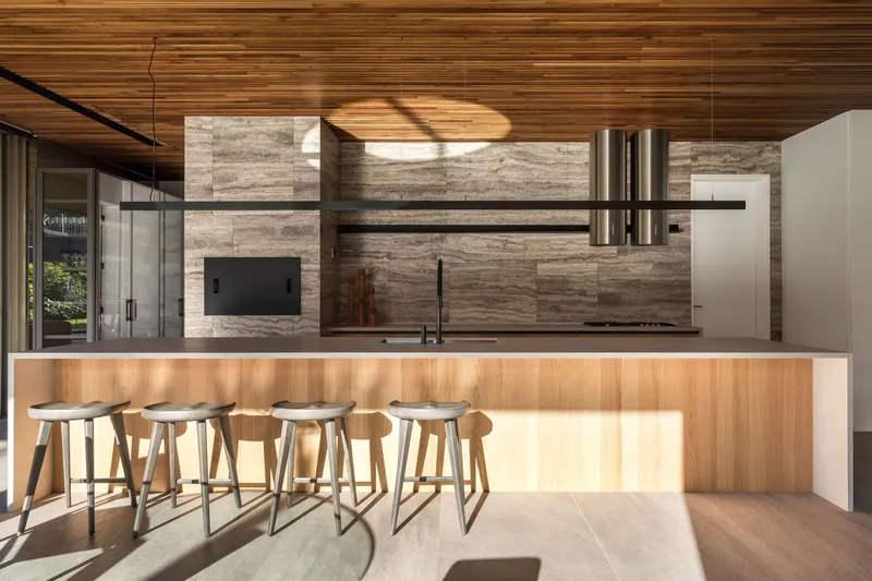 Kitchen island with timber base illuminated by afternoon light beneath a striated travertine feature wall