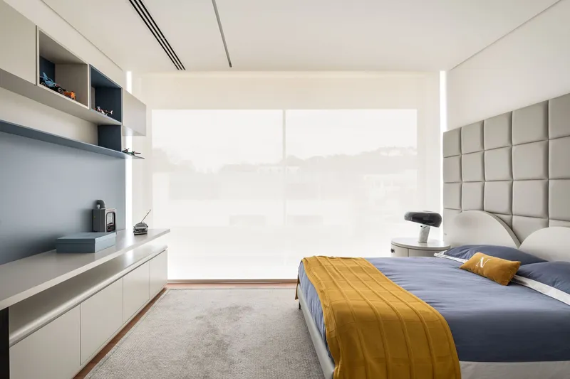 Bedroom with upholstered headboard and mustard throw facing a translucent window wall in soft daylight