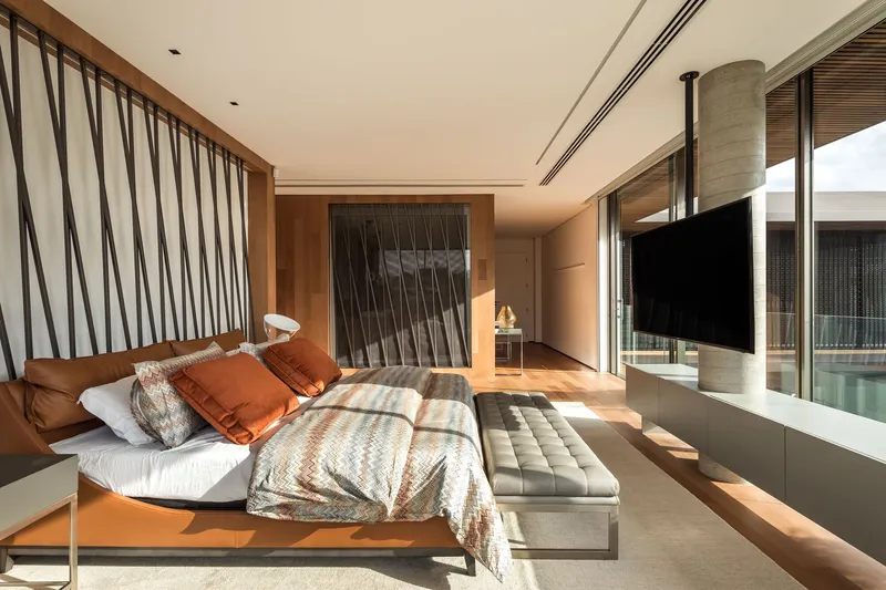 Bedroom with diagonal timber slat screen and glass wall opening to pool terrace in warm sunlight