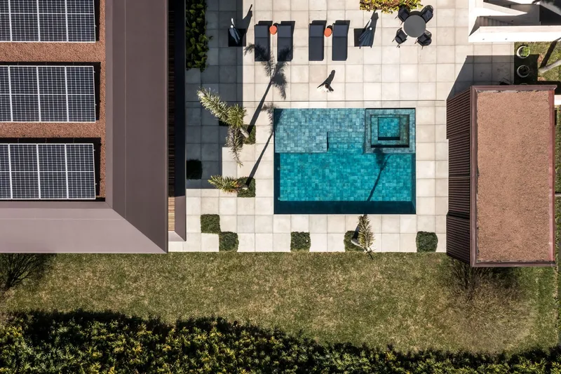Aerial view of the tiled pool deck with lounge furniture surrounded by white pavers and landscaped beds