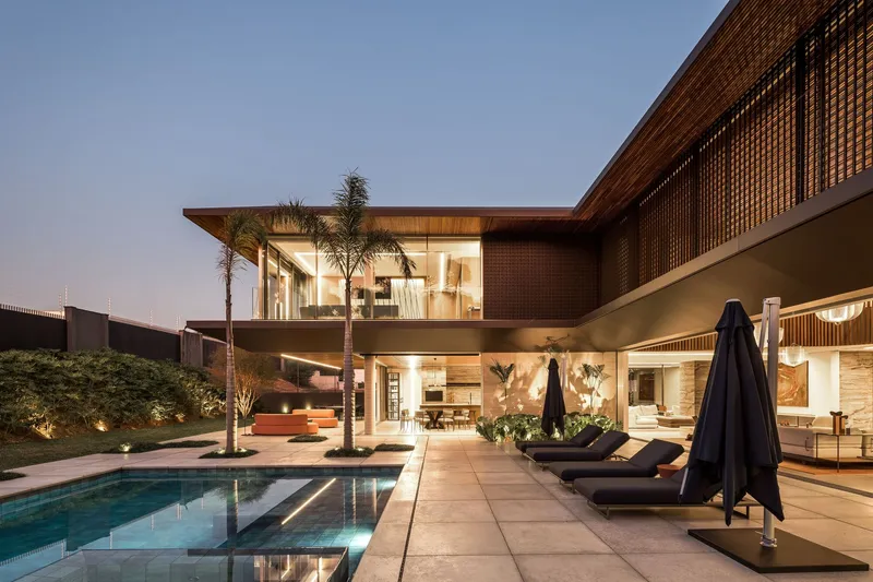 Pool terrace with glazed facades and timber screen walls illuminated at dusk