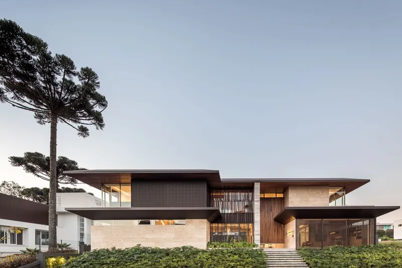 Street view showing layered horizontal volumes with timber screens and stone cladding at twilight