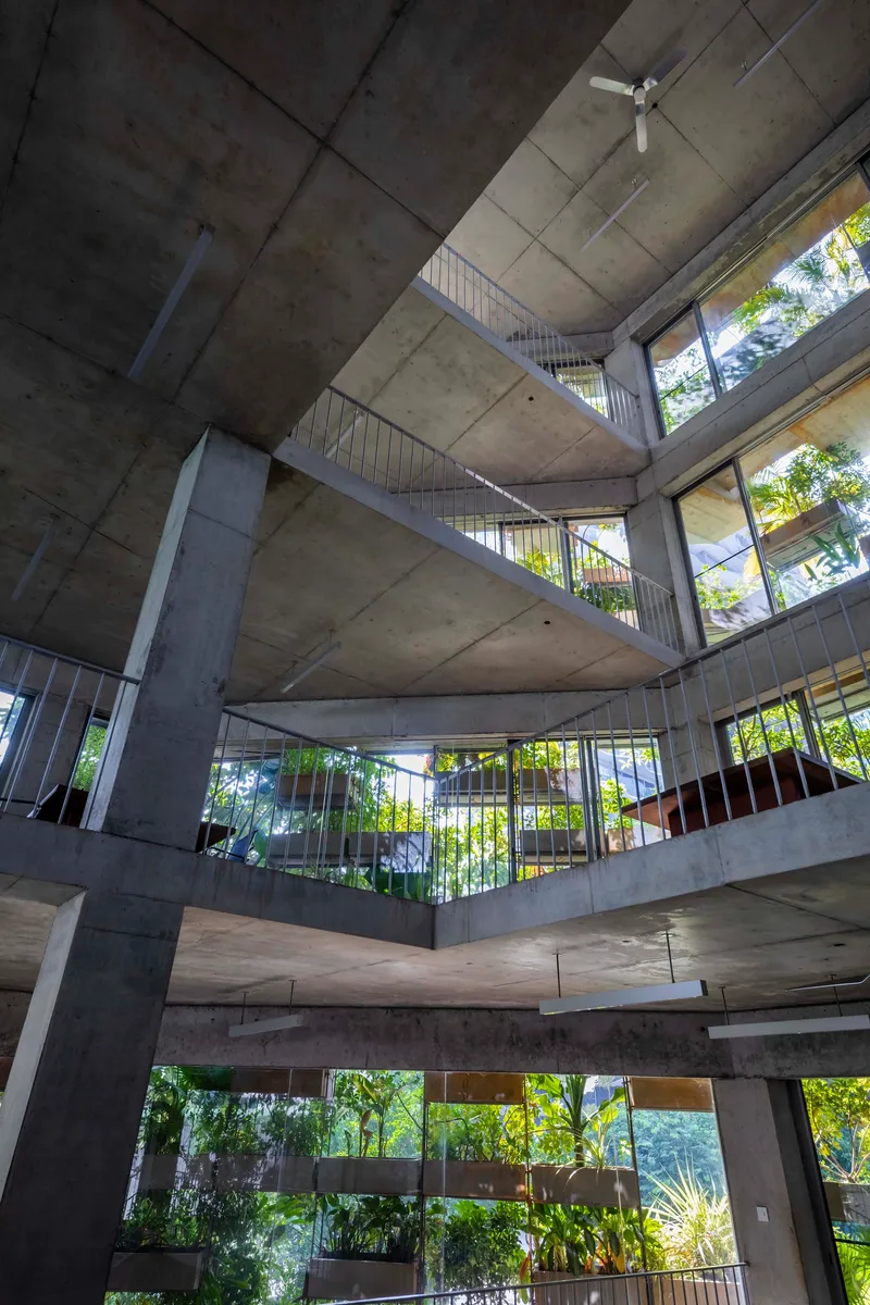 Upward view into the exposed concrete atrium with stacked balconies framing green trees beyond
