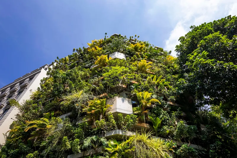 Street view of the planted facade with palms and ferns spilling from cantilevered concrete balconies