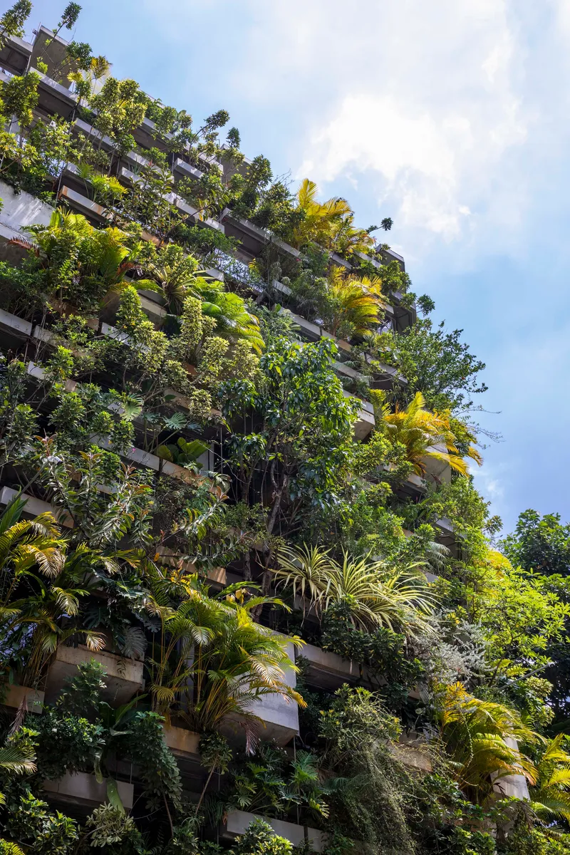 Facade with cascading greenery on every balcony rising against a partly cloudy afternoon sky