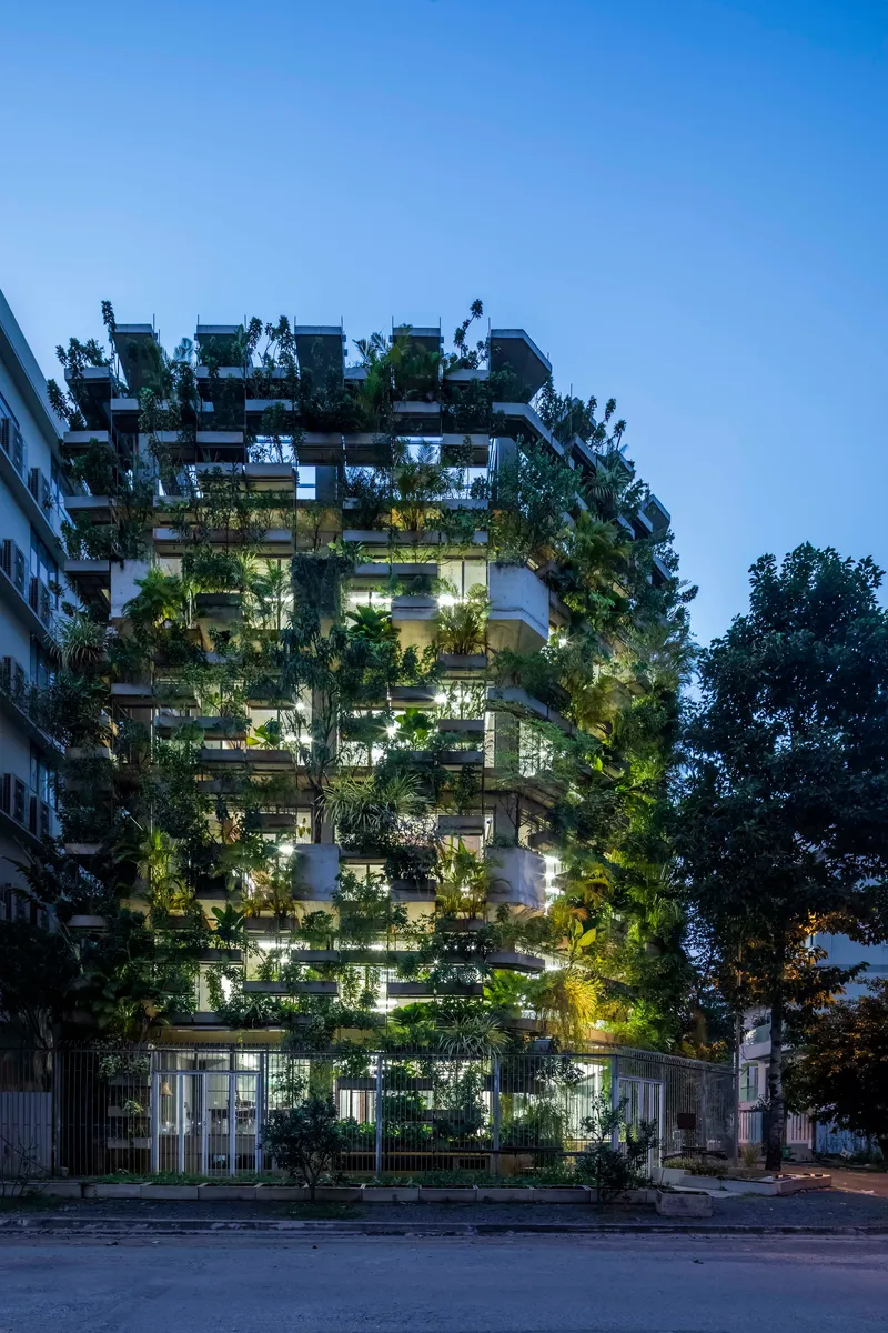 Street facade of the tower densely planted with trees on every balcony at twilight