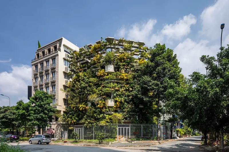Street corner view of the planted facade tower rising behind tree-lined sidewalks under afternoon clouds