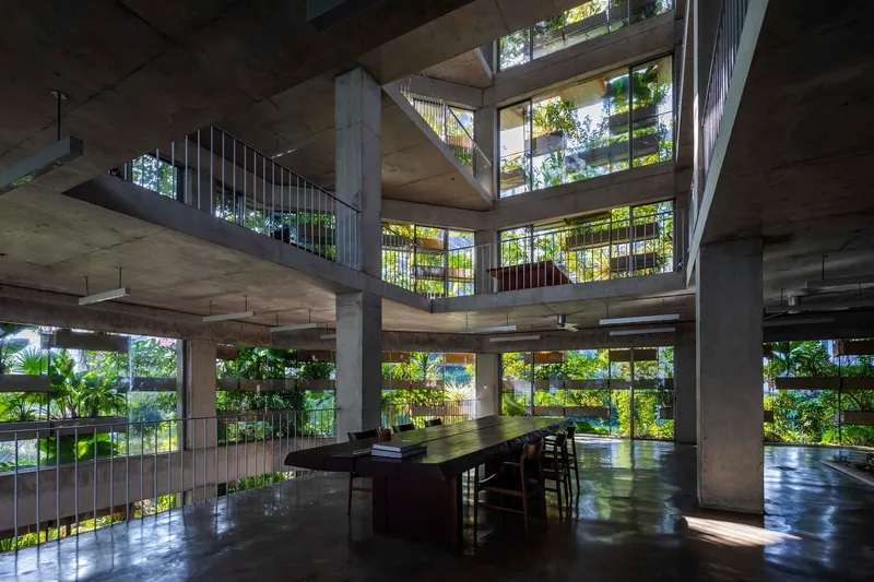 Interior atrium with concrete columns and cantilevered floors framing planted balconies in dappled sunlight