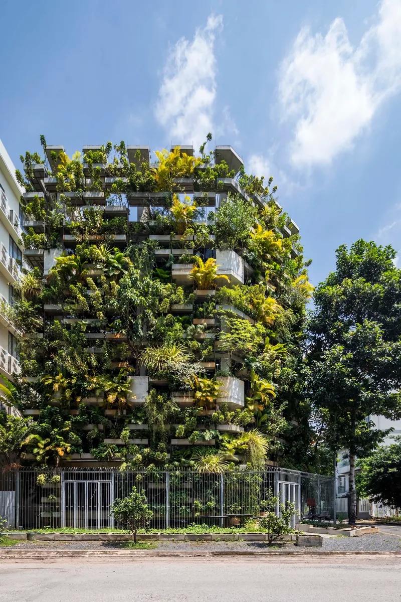 Street view of the planted balcony facade covered with dense tropical vegetation under blue sky