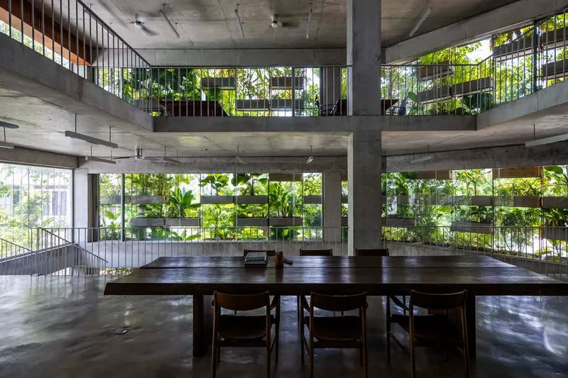 Dining table with wooden chairs beneath exposed concrete beams and planted terraces framed by vertical greenery
