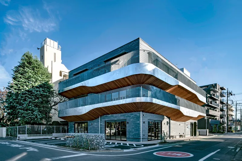 Street corner view of the layered facade with timber soffits and gabion walls under clear blue sky