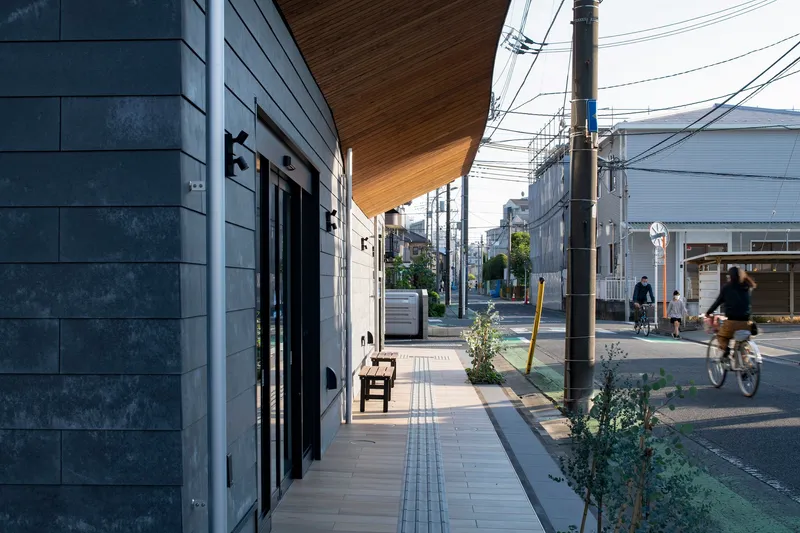 Covered sidewalk beneath the timber soffit with cyclists passing on the residential street at dusk