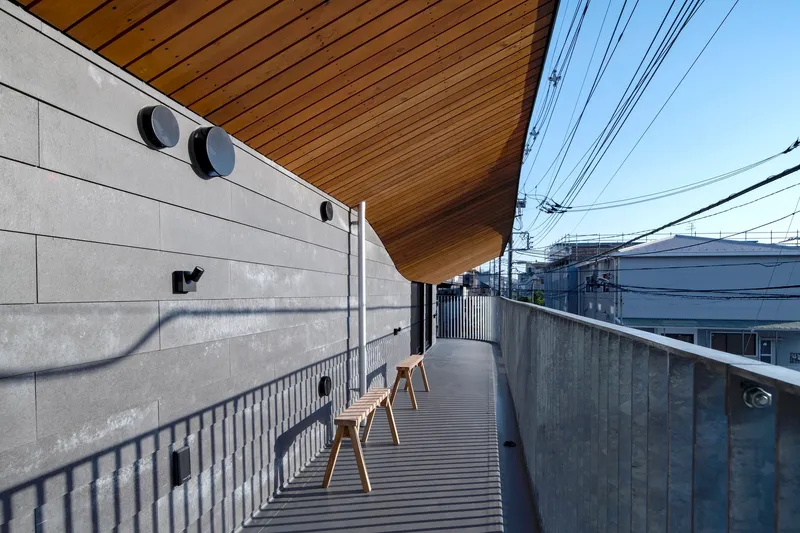Upper level terrace with timber slat decking and wooden stools beneath the cantilevered wood ceiling