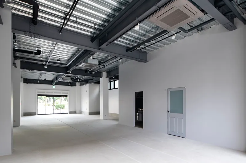 Interior space with exposed structural ceiling and white partition wall under ambient daylight