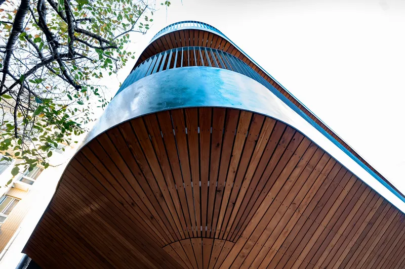 Upward view of the rounded balcony corner clad in vertical wood slats with metal edge trim