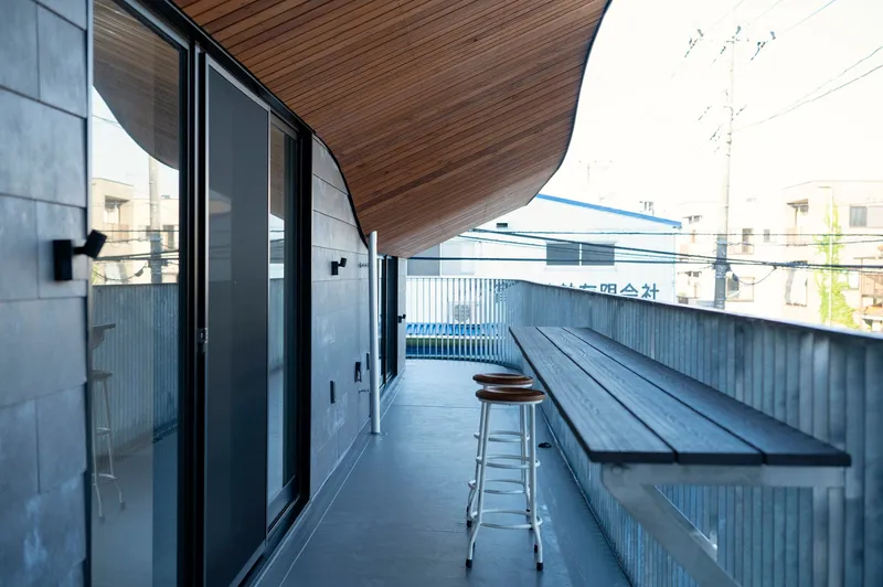 Narrow terrace with corrugated metal wall, black bench, and timber soffit above glass doors