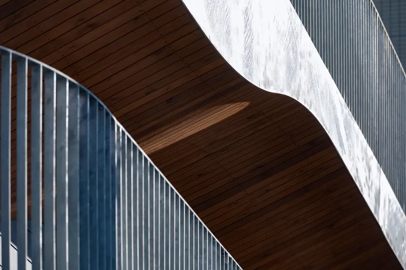 Detail of curved wood soffit meeting vertical metal slat wall in bright afternoon sunlight