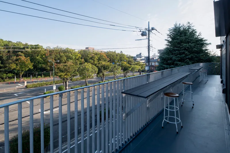 Terrace with vertical metal railing and folding bench overlooking a tree-lined street in afternoon light