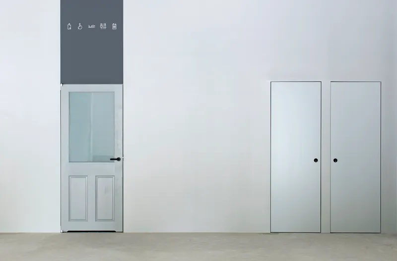 White wall with paneled door and pair of tall storage doors beside polished concrete floor