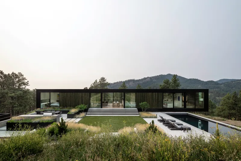 Black vertical cladding facade with full-height glazing overlooking a green roof and distant mountains under overcast skies