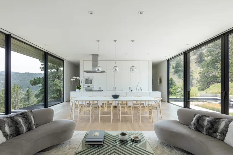 Open-plan kitchen and dining area flanked by floor-to-ceiling glazing with views to forested hills