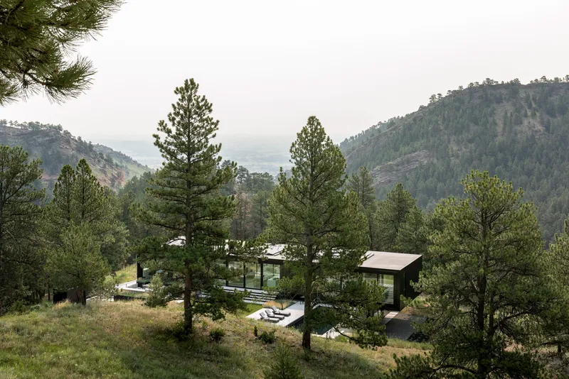Hillside view of the residence nestled among pine trees with mountain ridges visible in the distance