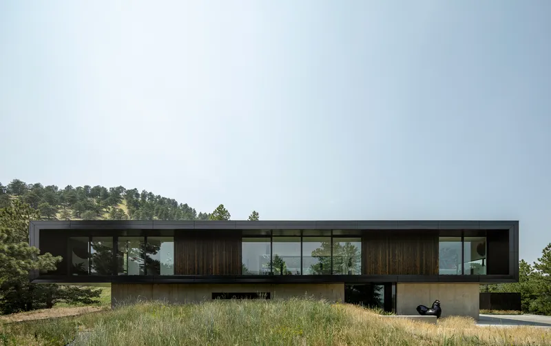 Long view of the dark timber and glass upper volume cantilevers over a concrete base in dry grassland