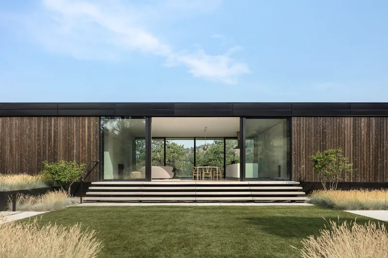 Wide concrete steps lead to the glazed facade with vertical timber cladding under an overcast sky
