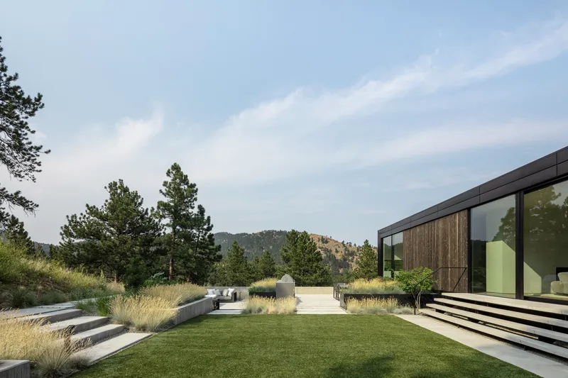 Terraced lawn and gravel pathway extend through native grasses toward forested hills beyond the glass facade