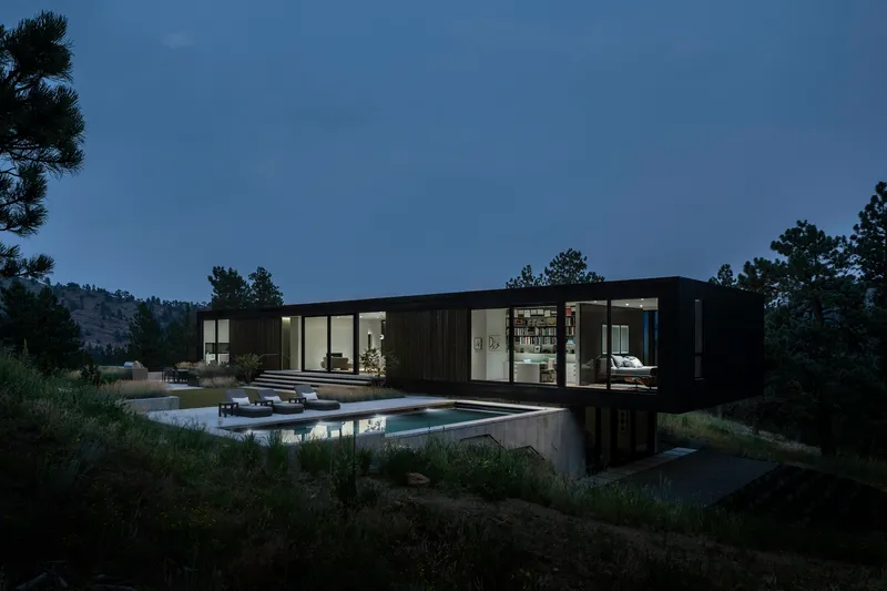 Black cladded residence with glazed openings above a concrete plinth and reflecting pool at twilight