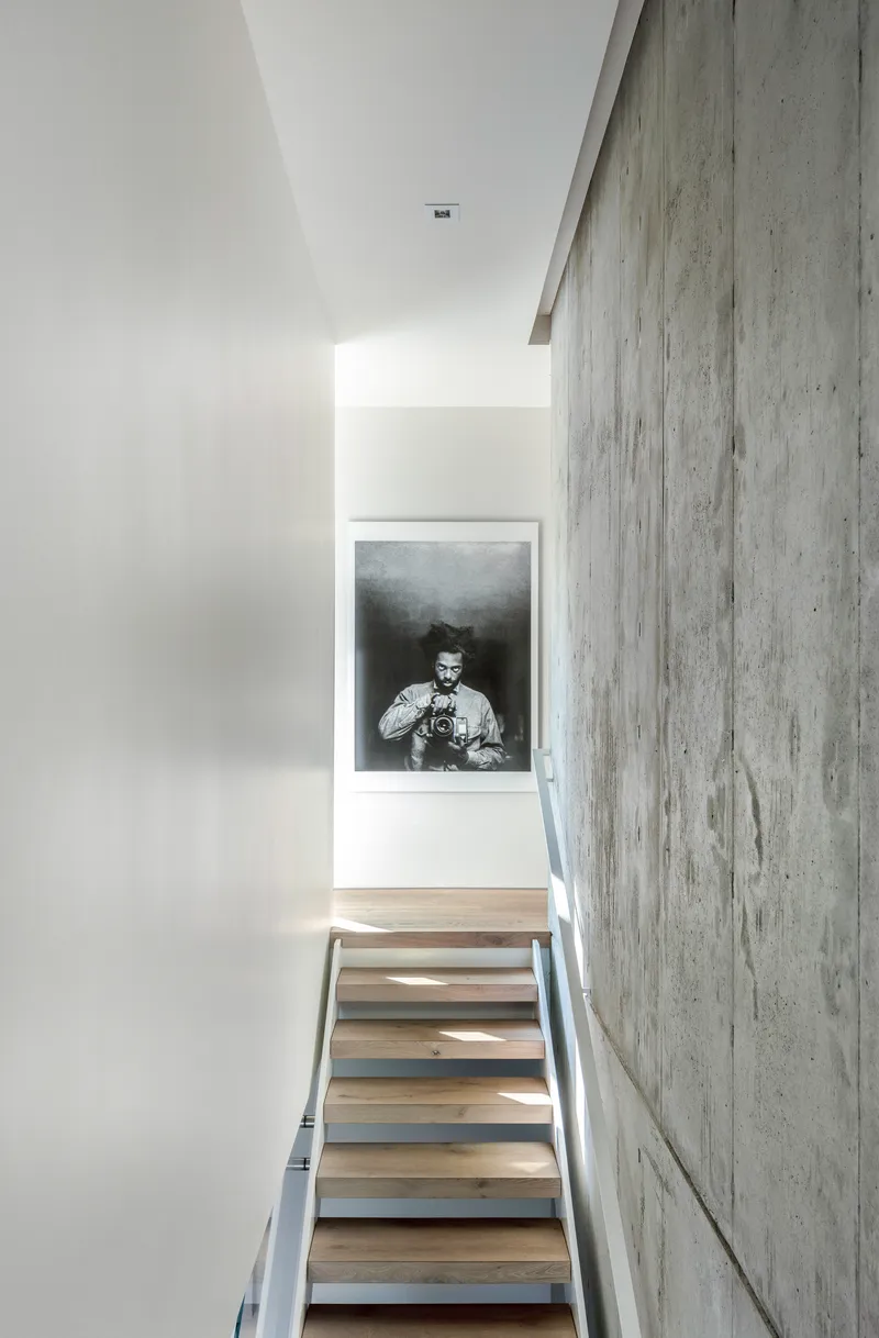 Staircase with floating timber treads alongside a board-formed concrete wall and framed photograph