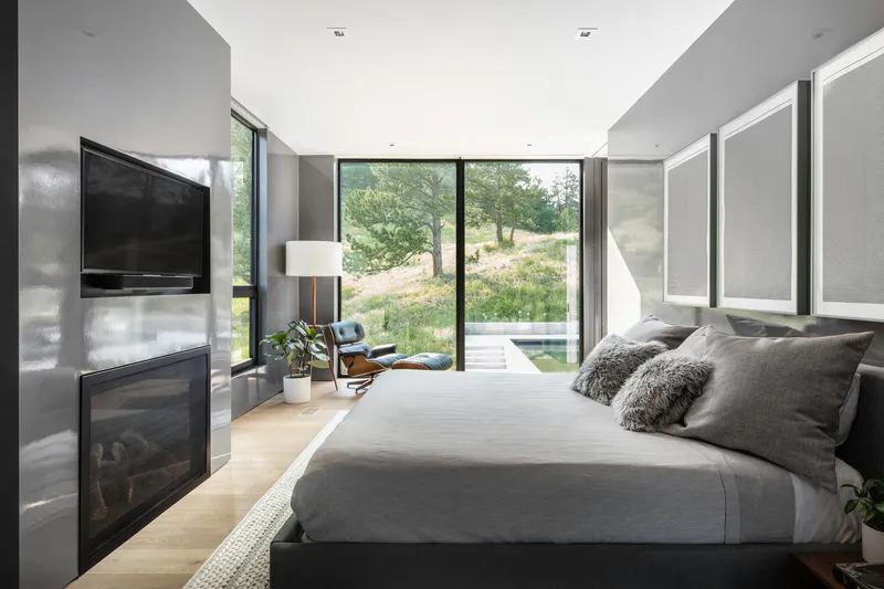 Bedroom with floor-to-ceiling glass doors opening to a grassy slope under afternoon light