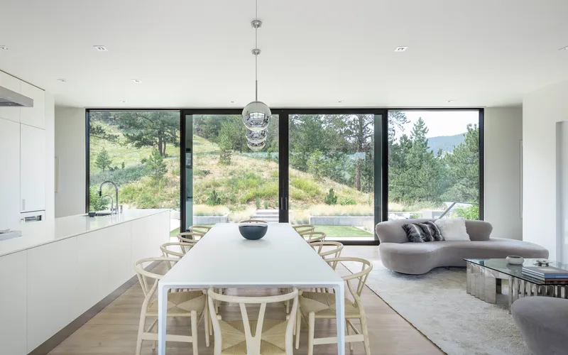 Open plan living and dining space with full-height glazing framing views of the hillside landscape