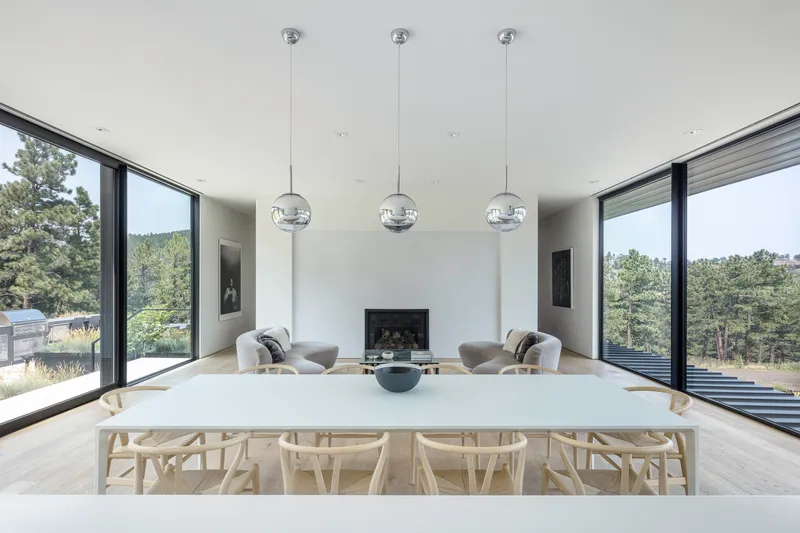 White dining table with wishbone chairs beneath three globe pendant lights and symmetrical corner windows