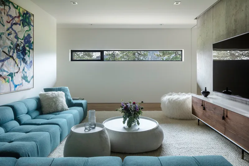 Living room with board-formed concrete accent wall and horizontal ribbon window framing foliage