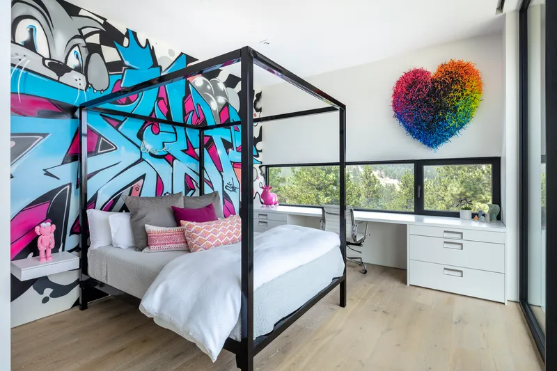 Bedroom with black canopy bed against a graffiti mural wall and ribbon window with shade