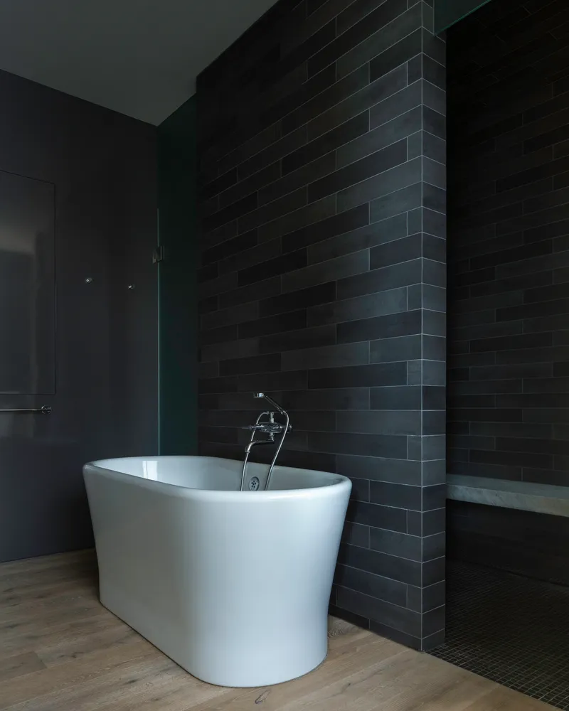 White freestanding bathtub against a dark brick tile wall in a dimly lit bathroom