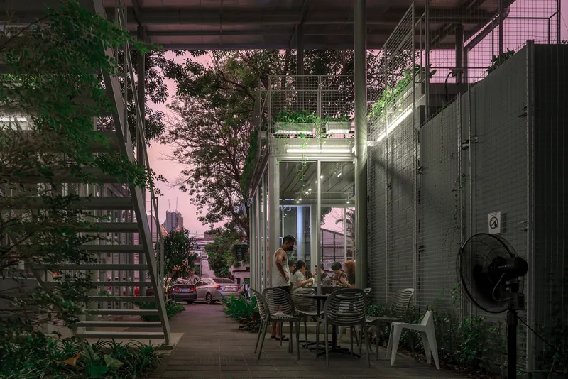 Covered ground-floor terrace with dining furniture surrounded by planted trees at twilight