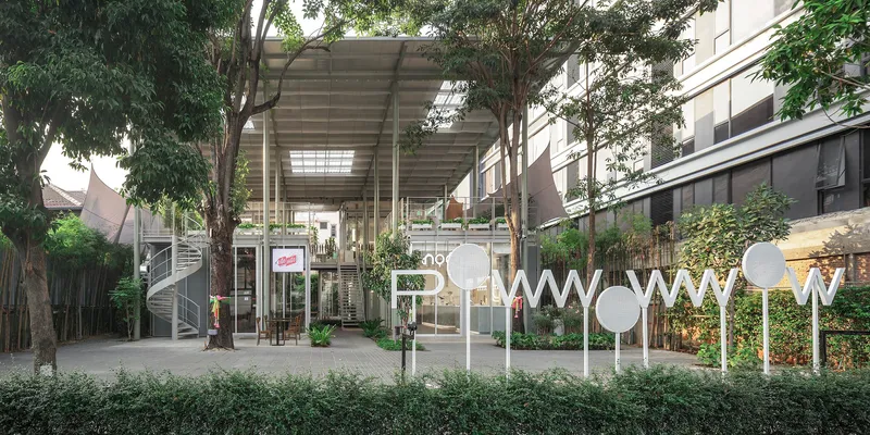 Courtyard view of the elevated pavilion with exposed steel structure and translucent roof panels framed by trees