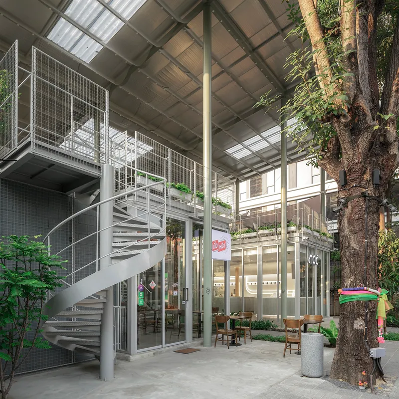Interior courtyard with a helical steel staircase, glazed volumes and a preserved tree with exposed roots
