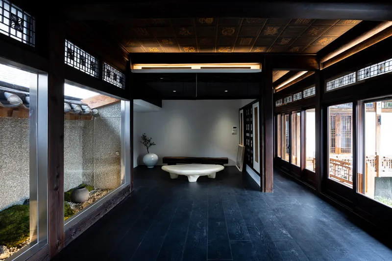 Interior corridor with dark timber frame and latticed transom windows overlooking a pebble courtyard