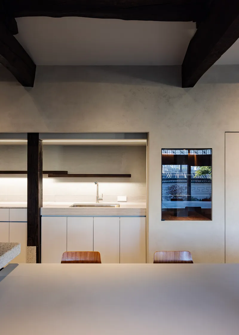 Kitchen with white cabinetry and backlit shelving beneath exposed timber beams and plaster ceiling