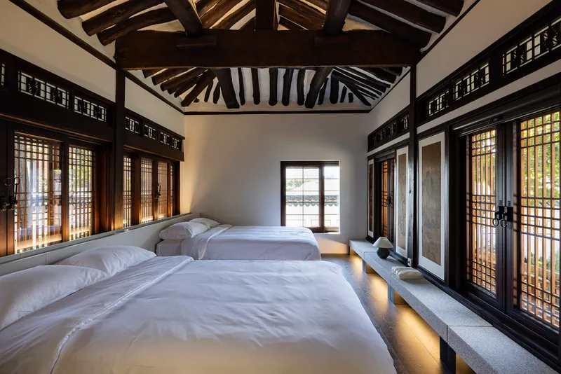Bedroom with twin platform beds, latticed door panels, and exposed timber roof trusses at dusk