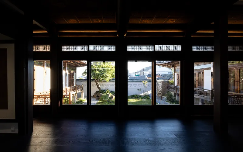 Interior room with timber lattice windows framing a courtyard garden visible in afternoon light