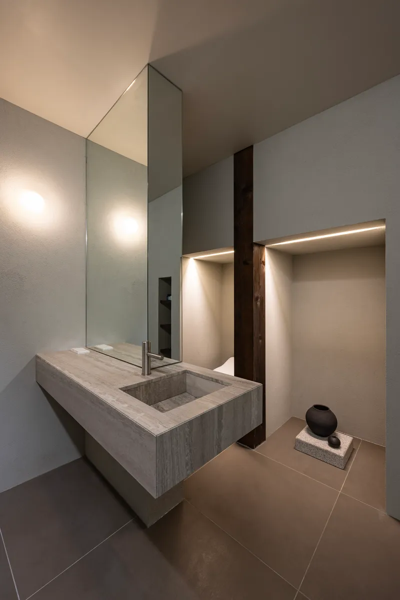 Concrete vanity basin with wall-mounted mirror and recessed lighting in a minimalist washroom