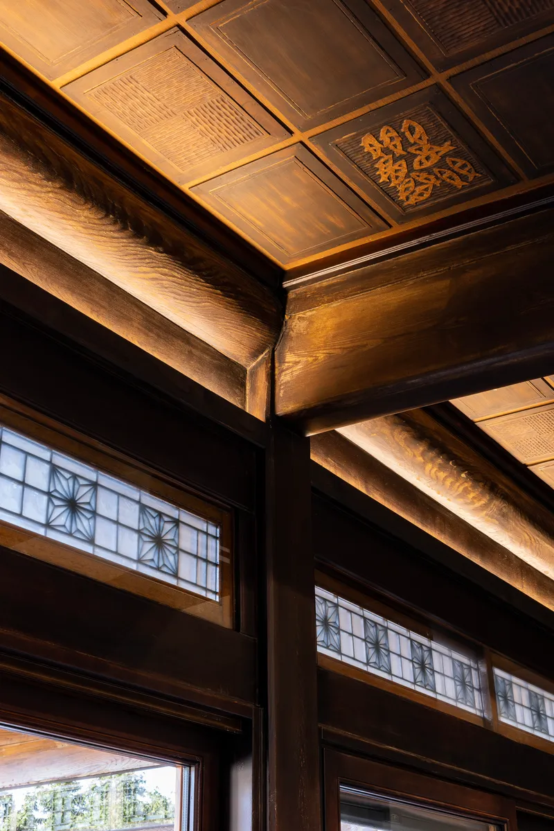 Upward view of timber ceiling beams with ornamental panels and lattice transom windows below
