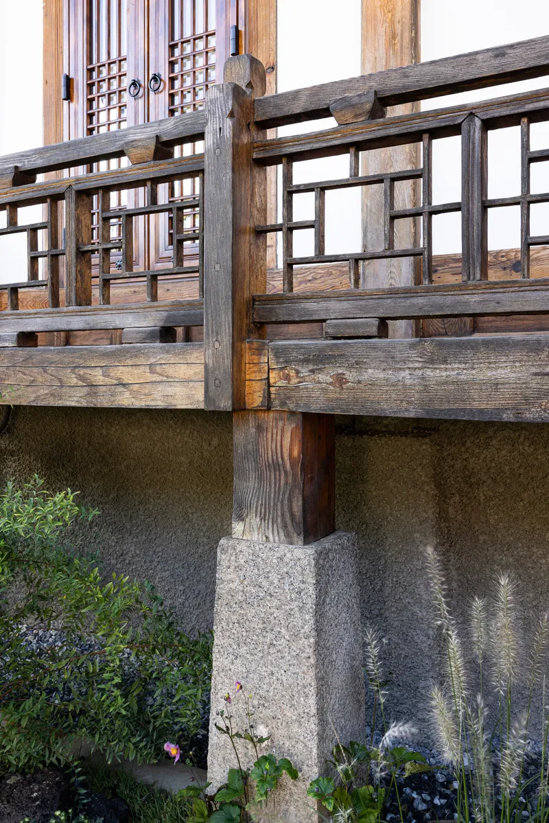 Timber balustrade on a stone plinth beside a planted bed with grasses and shrubs