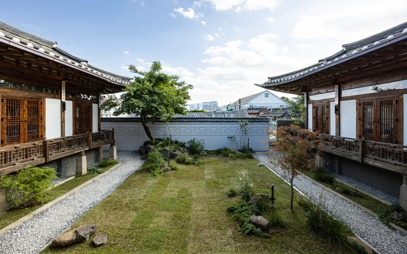 Central courtyard garden with gravel paths between two timber-framed pavilions under a cloudy sky