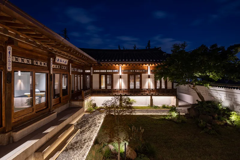 Traditional timber pavilions framing a courtyard garden with low plantings under a deep blue night sky